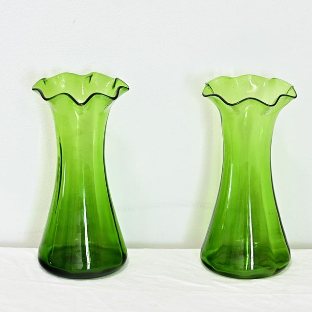 A delightful pair of large, green glass hyacinth vases from Victorian England, late 19th century. The ruffled mouth (where...