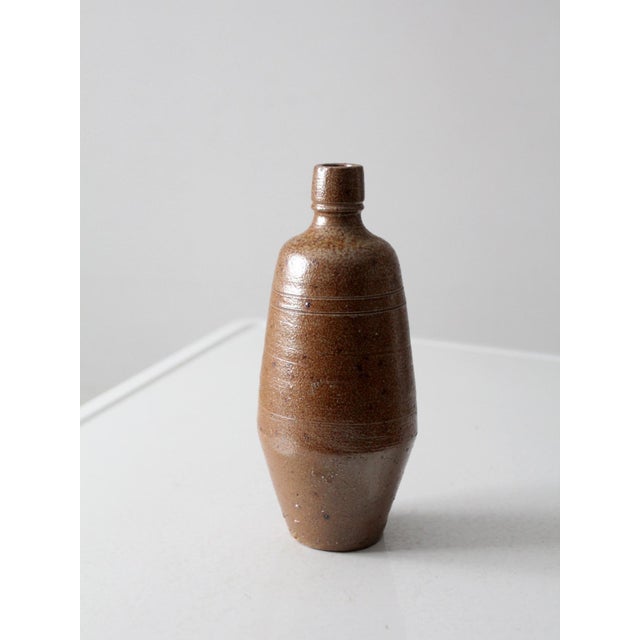 A vintage handmade studio pottery vase with a tall, tapered form and narrow bottleneck opening. Finished in a warm brown...