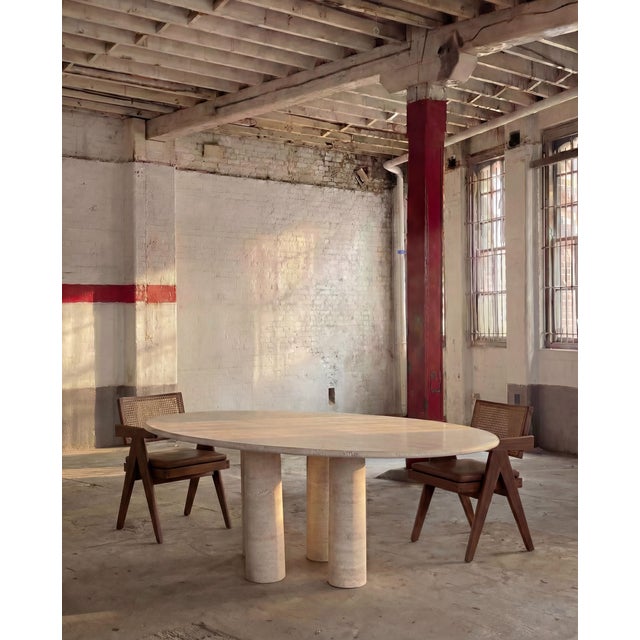 This minimalist dining table is crafted entirely from solid stone and rests on four gently tapered cylindrical columns,...