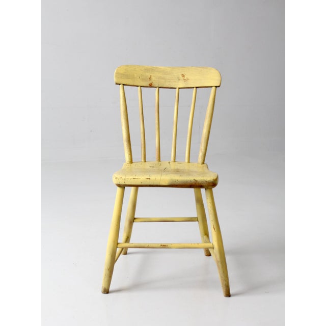 An antique primitive plank seat chair dating to the early 20th century, featuring a shaped wooden seat, tapered legs, and...