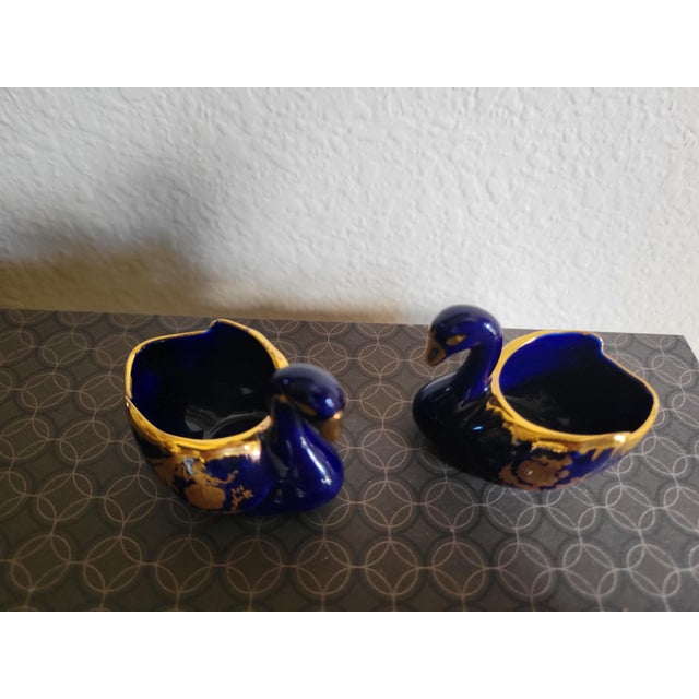 A refined pair of Limoges porcelain swans, crafted in deep cobalt blue and finished with hand‑applied 22 Karat gold gilt...