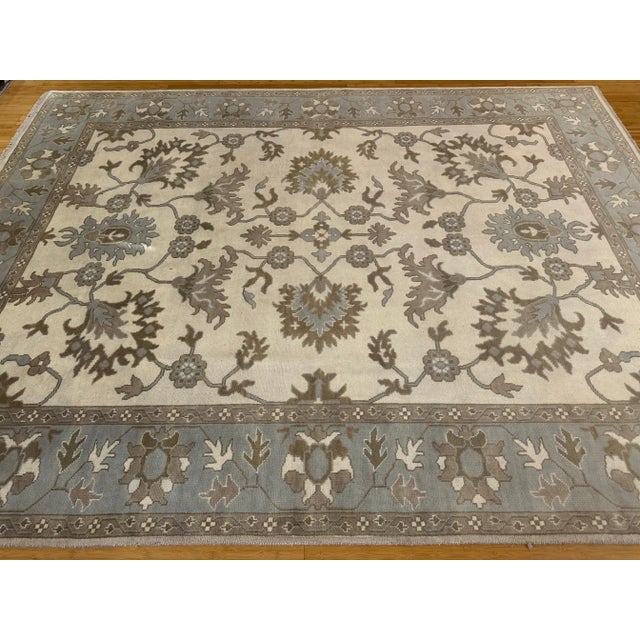 A large handmade Serapi-style rug measuring 9'1 x 11'11, featuring a light, airy palette of beige, ivory, and soft slate...