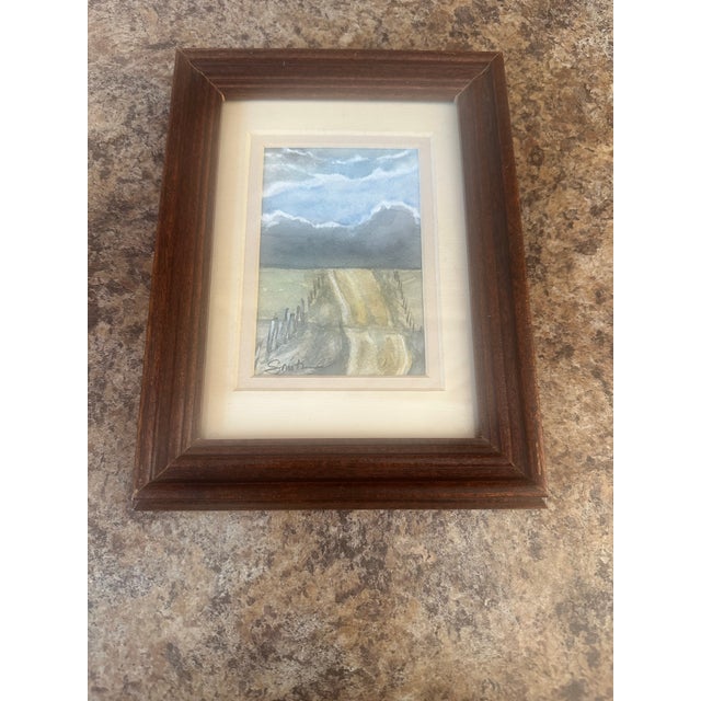 Original watercolor landscape featuring a rural dirt road stretching toward the horizon beneath dramatic, cloud-filled...