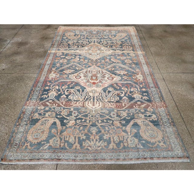 This early 20th-century Persian Bakhtiari carpet presents a richly detailed tribal composition across a deep blue field....