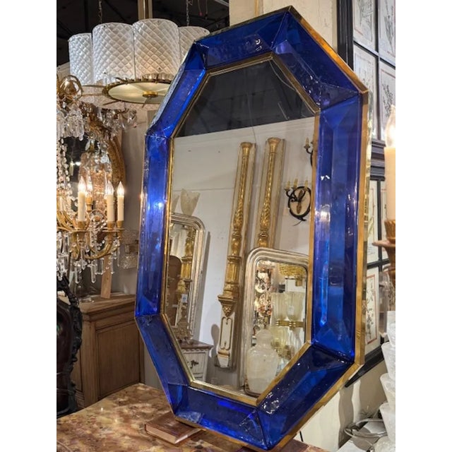 The product is a modern cobalt blue Murano glass octagonal mirror with brass details. The glistening glass adds a real...