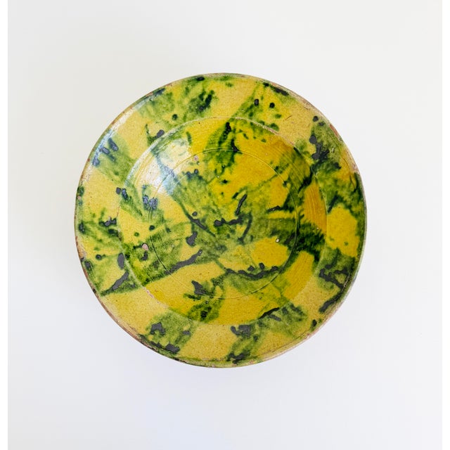 An antique 19th century earthenware bowl with hand-painted yellow and green freeform brushwork. Crafted from a warm...