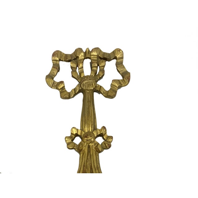 A set of three small gilt Rococò style mirrors: (i) one with an oval frame topped with a carved bow and ribbon motif and a...