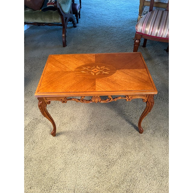 A vintage French Provincial Louis XV style coffee table featuring an elegant floral marquetry inlay medallion within a...