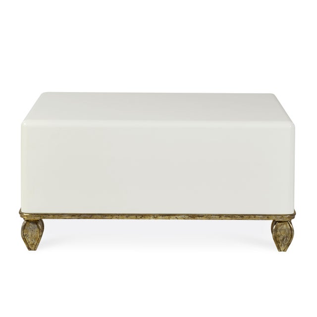 The contemporary high gloss cream lacquered ottoman coffee table featuring mid-century inspired feet, showcases a fusion...