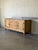 This low sideboard features a central stack of three drawers flanked by two side doors opening to interior shelving. A...