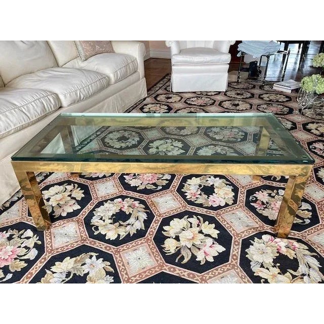A Mid Century Karl Springer style rectangular coffee table with brass base structure topped with a thick piece of clear...