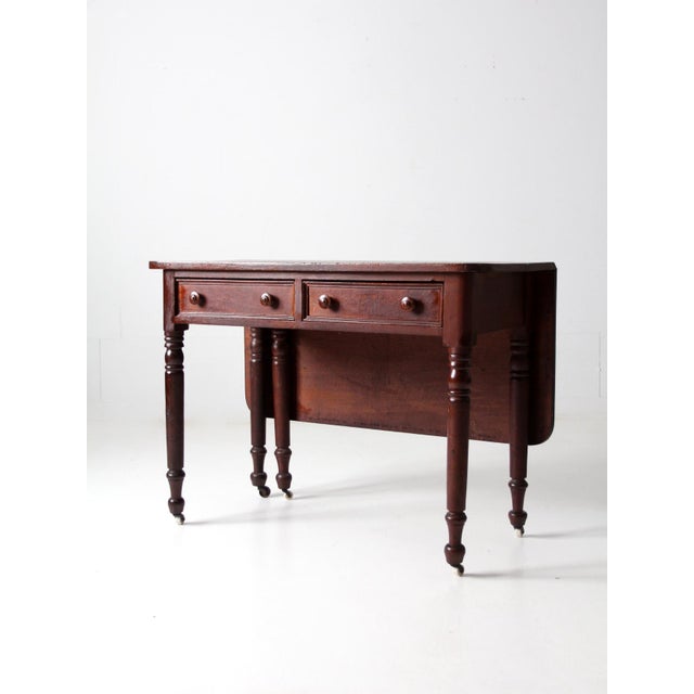 This is a 19th century antique writing desk with drop leaf extension. The wood desk features two drawers and turned legs...