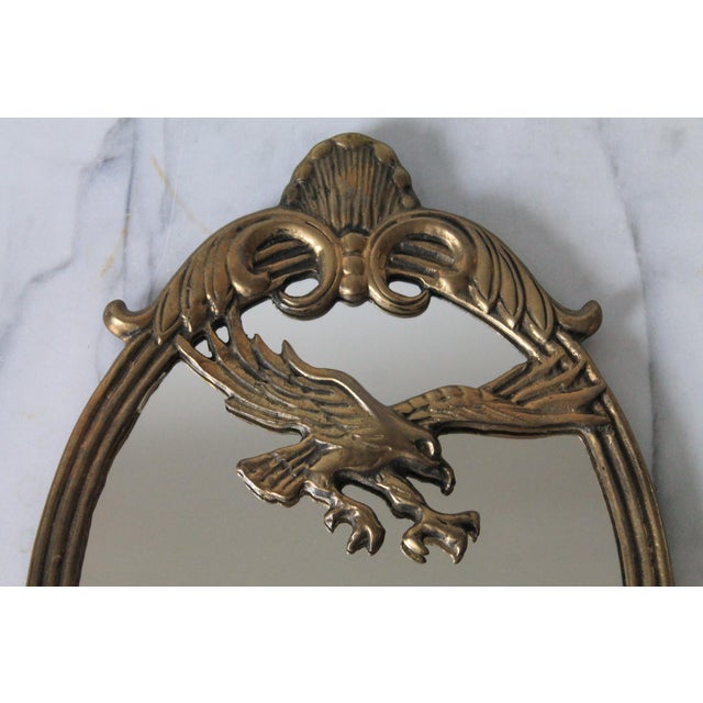 Vintage brass oval wall mirror featuring an ornate American Federal-style eagle motif across the upper center. Made in...