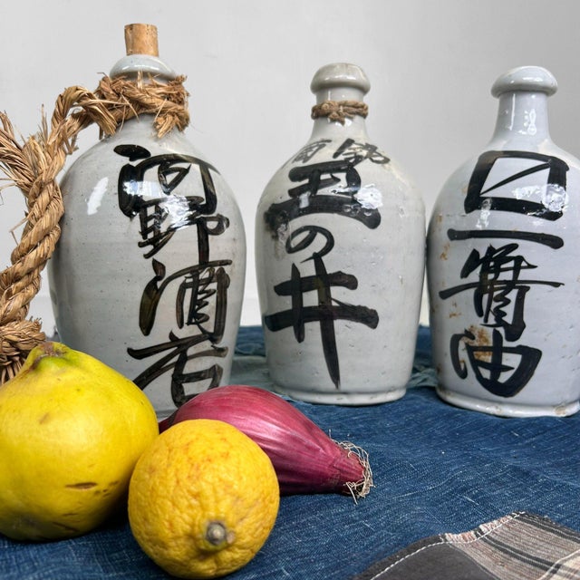 Three distinctive earthenware jugs with a soft gray-white glaze and bold, hand-painted calligraphy: two in deep black and...