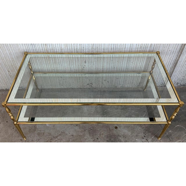 About Mid-Century Modern two-tier brass and mirror beveled glass side table in Maison Jansen style with fluted brass legs...