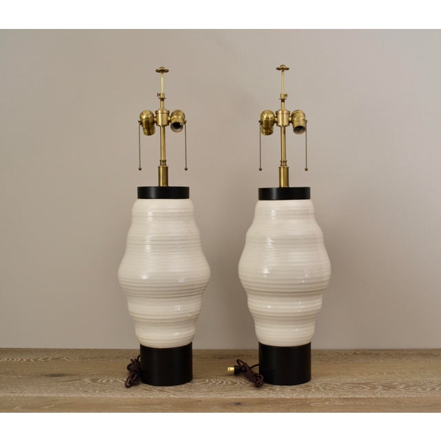 Beautiful pair of modernist designer table lamps in crackled ceramic in a modern ribbed form over large wood bases. Satin...