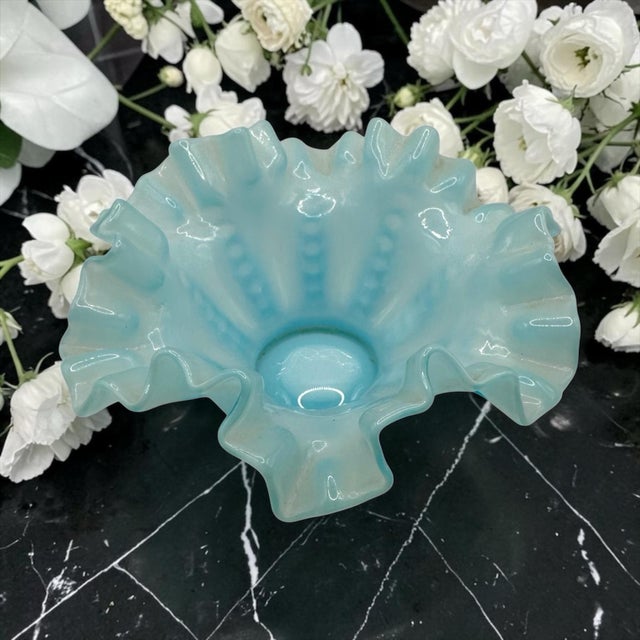 This blue opalescent ruffled bowl featuring crimped edge design and delicate color transitions from translucent blue to...
