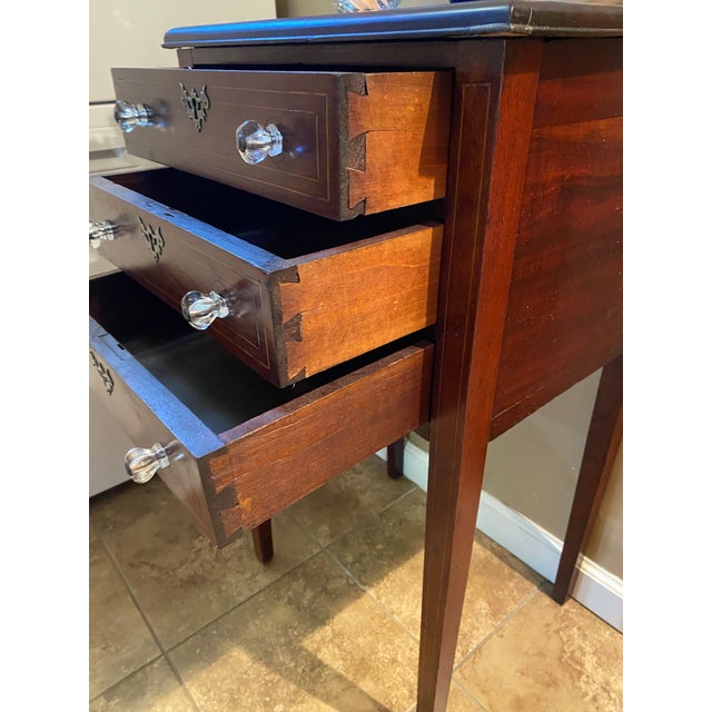 Elegant mahogany nightstand has a dark reddish-brown finish with decorative light wood string inlay on the top and drawer...