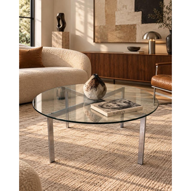 Sleek 1970s Mid-Century Modern round coffee table featuring a clear glass top supported by a sculptural chrome X-form...