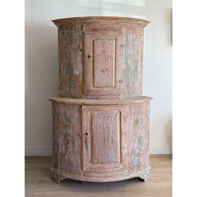 This antique Swedish corner cupboard is a striking study in form and age. Designed to nest into a corner, its rounded...
