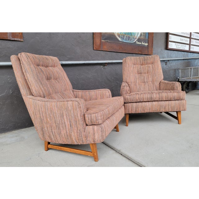 A pair of Mid-Century Modern high-back upholstered lounge chairs with exposed wood base. Appear to have an older re-...