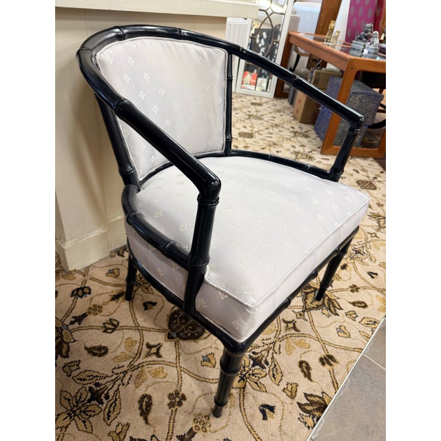 A chic and timeless faux bamboo chinoiserie accent chair featuring a gracefully curved barrel back frame in glossy black...