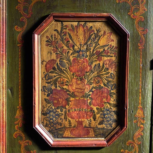 This antique painted armoire in pine wood retains its original polychrome over a green ground, with four painted panels of...