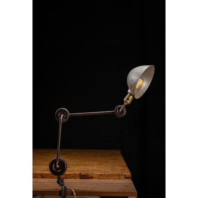 Industrial articulating task lamp featuring a heavy cast iron clamp base, dual articulating steel arms, and a spun...