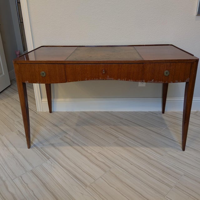A striking French 1930s writing desk featuring an elegant, gently curved apron, tapered legs, and an inset leather writing...