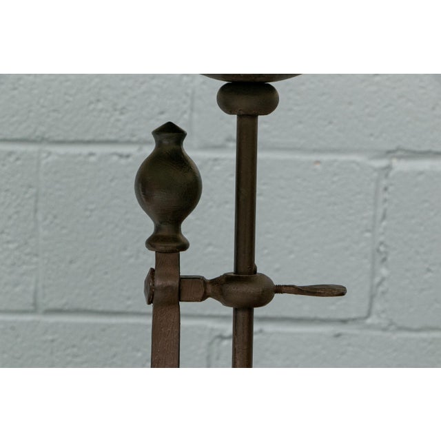 A vintage wrought iron floor lamp with a tapered lampshade, wide and sturdy tripodal base, slender shaft with decorative...