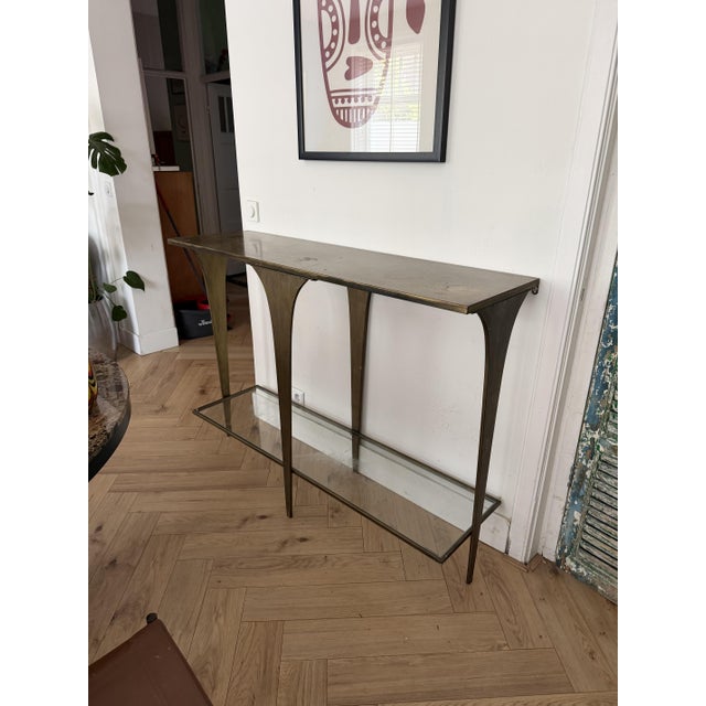 A sculptural wall-mounted console table in solid brass, featuring dramatically flared, trumpet-shaped legs that taper from...