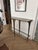 A sculptural wall-mounted console table in solid brass, featuring dramatically flared, trumpet-shaped legs that taper from...