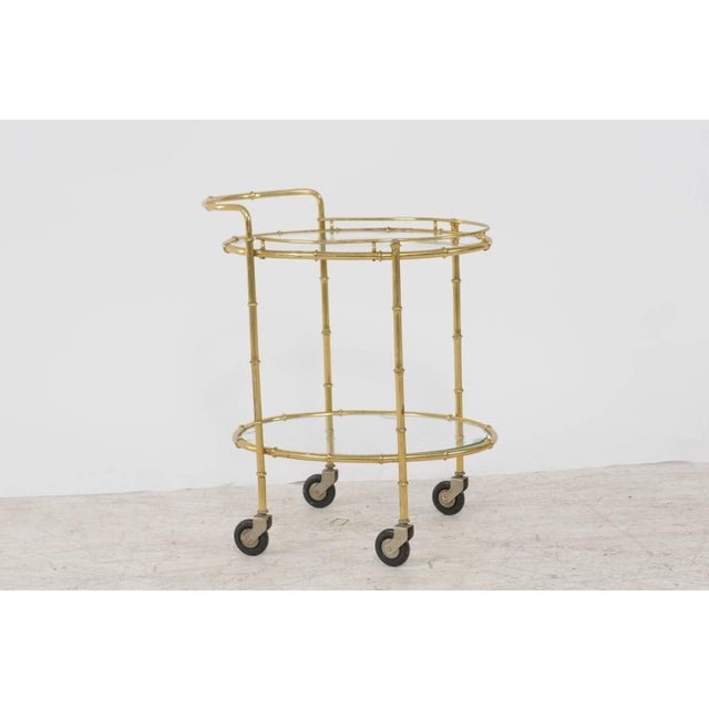 A French vintage brass cart from the 1950s with glass oval shelves and casters. Born during the mid-20th century, this...