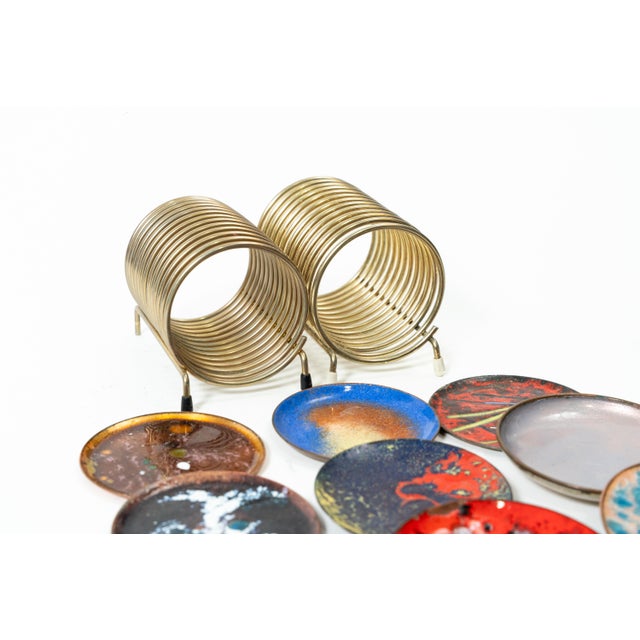 The objects pictured are vintage enamel coasters (or small plates) made of copper, arranged in a spiral metal stand. Such...