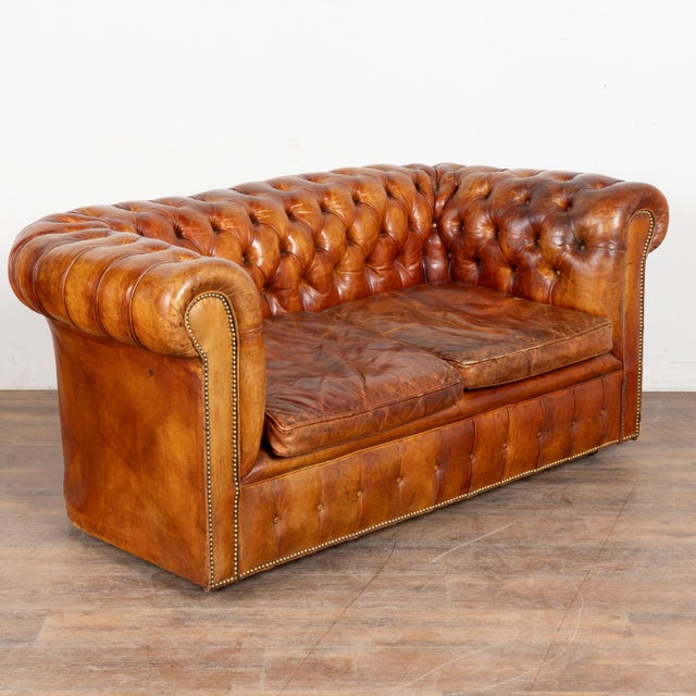 Pair of French Chesterfield two seat loveseat sofas upholstered in vintage brown leather. This handsome pair features...