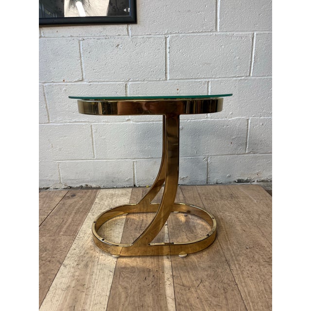 A striking Postmodern side table executed in polished brass with a thick circular glass top. The sculptural pedestal base...