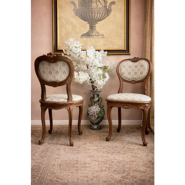 An elegant pair of early 19th century French salon chairs, distinguished by their shaped backs, finely carved aprons, and...