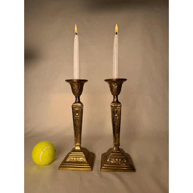 The motifs of sashes, bows and ribbon decorate the trapezoid shaped columns of this pair of solid brass candlesticks....