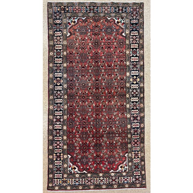 Hand-knotted runner from the Hamadan region of western Iran, featuring a dense allover geometric pattern set within a red...