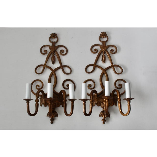 Vintage pair of gold-finished wall sconces with intricate scrolling arms and candle covers. Cast metal with a distressed...