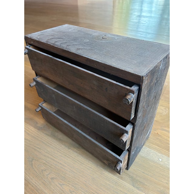 This is a miniature chest of drawers made in a primitive style. The wood is probably pine stained a dark color. The...
