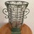 This large hand-blown caged glass footed vase features a wrought iron frame with scroll handles, making it a decorative...