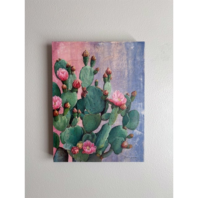 This oil painting depicts a vibrant cluster of prickly pear cacti adorned with delicate pink flowers, showcasing the...