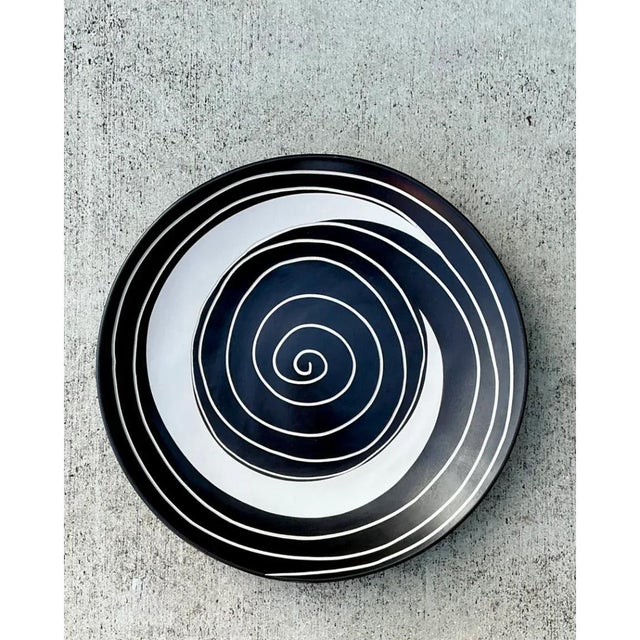 This oversized decorative plate makes an unmistakable graphic statement through its bold, hypnotic spiral motif, a...