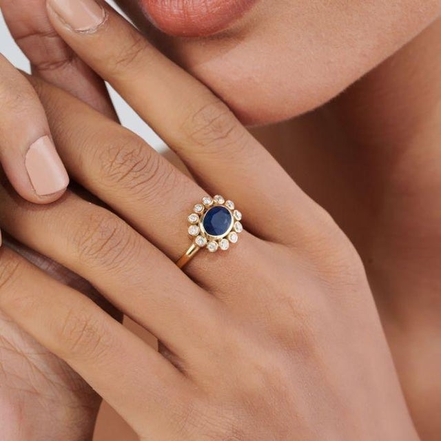 This halo cluster ring features a striking 1.83ct oval cut blue sapphire, set in 14K yellow gold. The center oval blue...