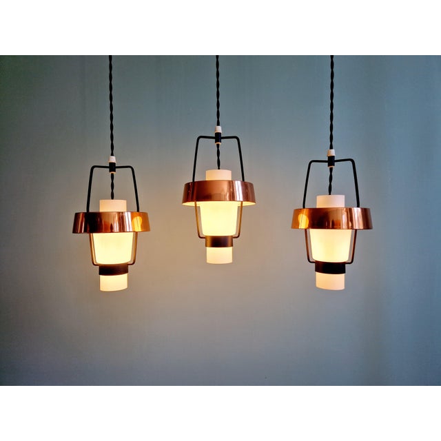 A trio of scandinavian pendant lights from the 1960s, each composed of a white opaline glass globe topped with a copper-...