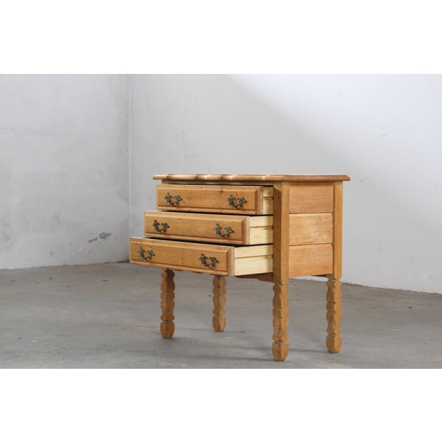 This oak side table, attributed to Danish designer Henning Kjærnulf, exemplifies the Brutalist aesthetic of the 1960s....