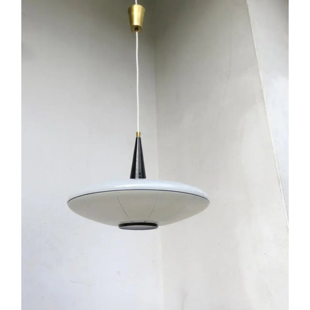 A "ufo" ceiling light from the 1950s, manufactured by doria werke. the white glass shade has a striped pattern with black...