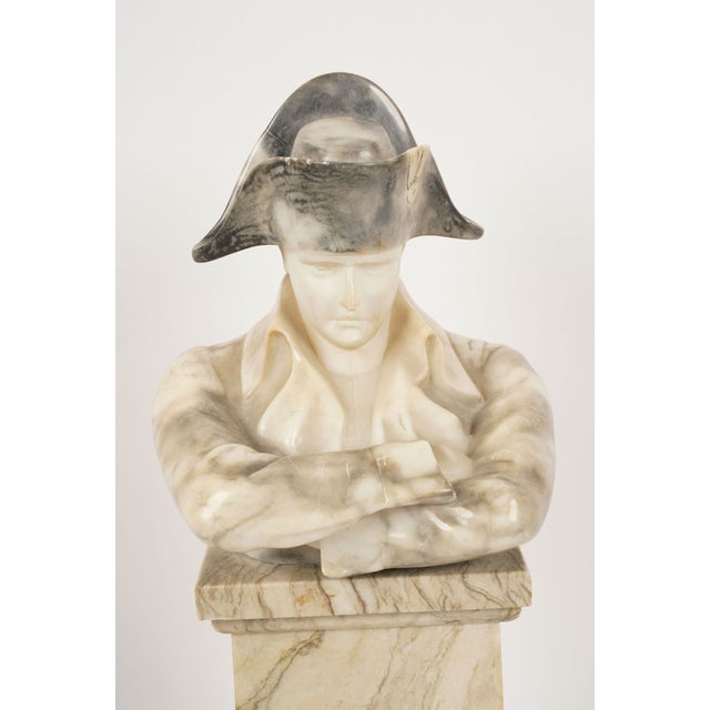 Depicted in his iconic bicorne hat and contemplative crossed-arm pose, Napoleon rests atop an architectural pedestal...