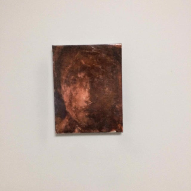 The artwork features an abstract representation of a face, rendered in deep, muted tones that evoke a sense of mystery and...